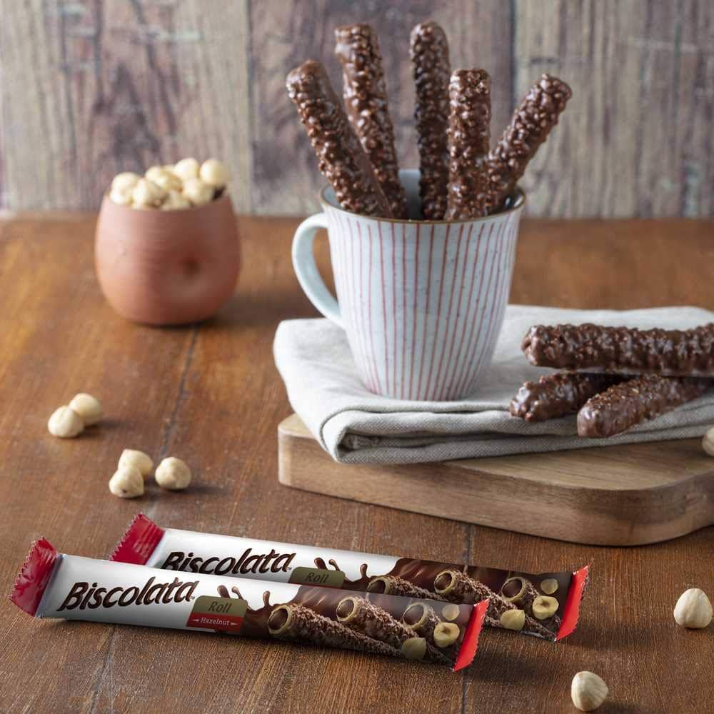 Chocolate-covered sticks in a mug on a wooden table with Biscolata bars in the foreground.